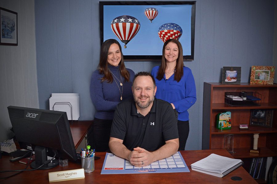 About Our Agency - The Leighton Insurance Agency Team Sitting and Standing Behind the Desk of their Office With Lots a Patriotic Theme